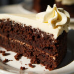 Whole chocolate cake covered in cream cheese frosting on a cake stand.